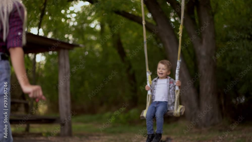 Mom blonde shakes her son on a swing tied to a tree in the park. Happy childhood Mom blonde shakes her son on a swing tied to a tree in the park. Happy childhood