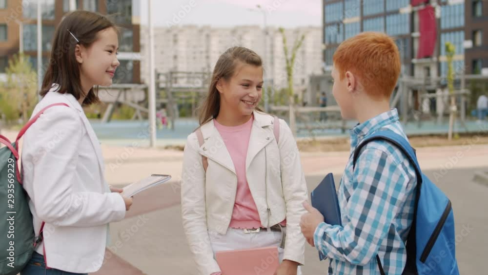 Medium shot of two multiethnic girls with notebooks in their hands standing and talking to ginger Caucasian boy wearing blue shirt Medium shot of two multiethnic girls with notebooks in their hands standing and talking to ginger Caucasian boy wearing blue shirt