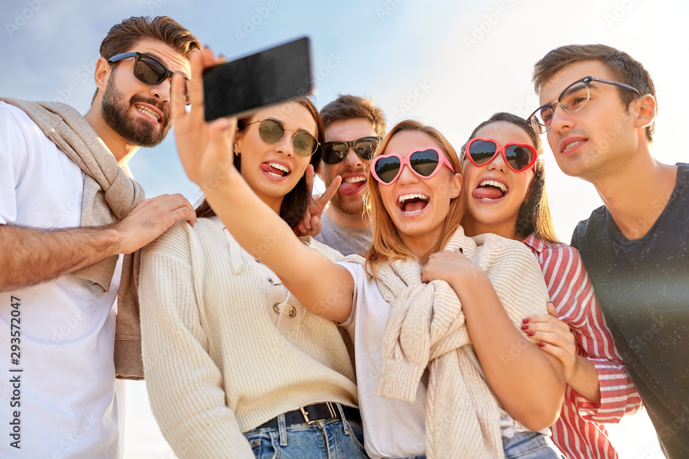 friendship, leisure and people concept - group of happy friends taking selfie by smartphone in summer