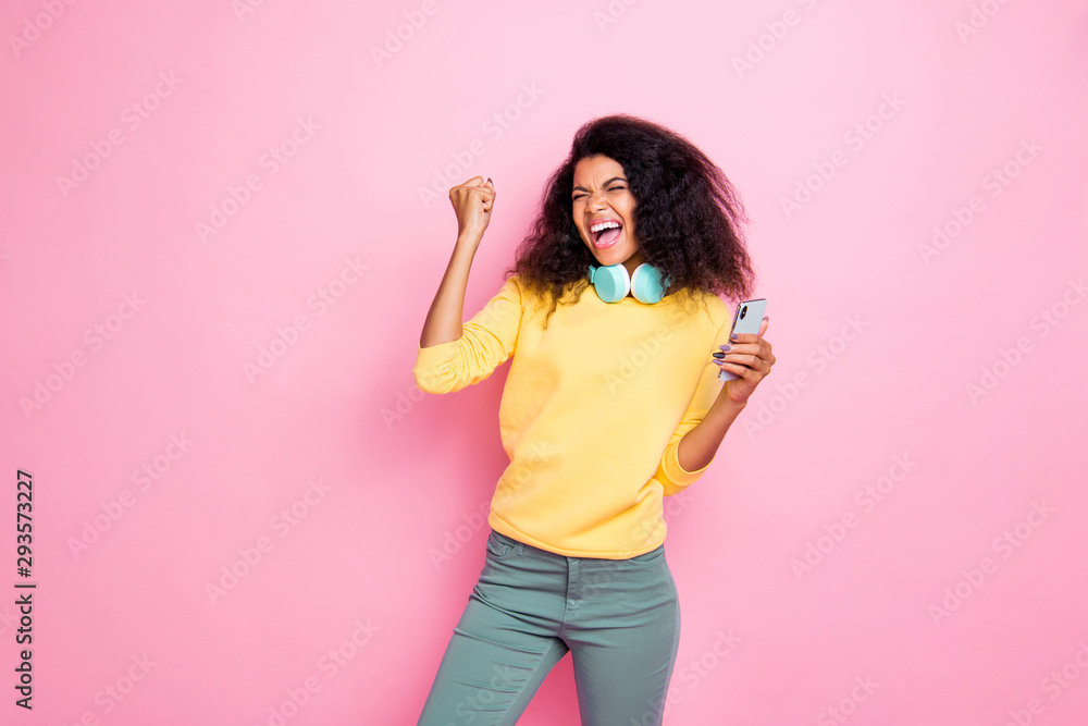 Portrait of crazy funky hipster african girl use cellphone get feedback from followers raise fists scream yes celebrate achievement wear yellow sweater pants isolated over pink color background Portrait of crazy funky hipster african girl use cellphone get feedback from followers raise fists scream yes celebrate achievement wear yellow sweater pants isolated over pink color background