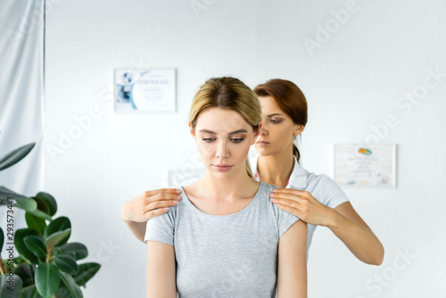 chiropractor touching shoulders of attractive patient in grey t-shirt