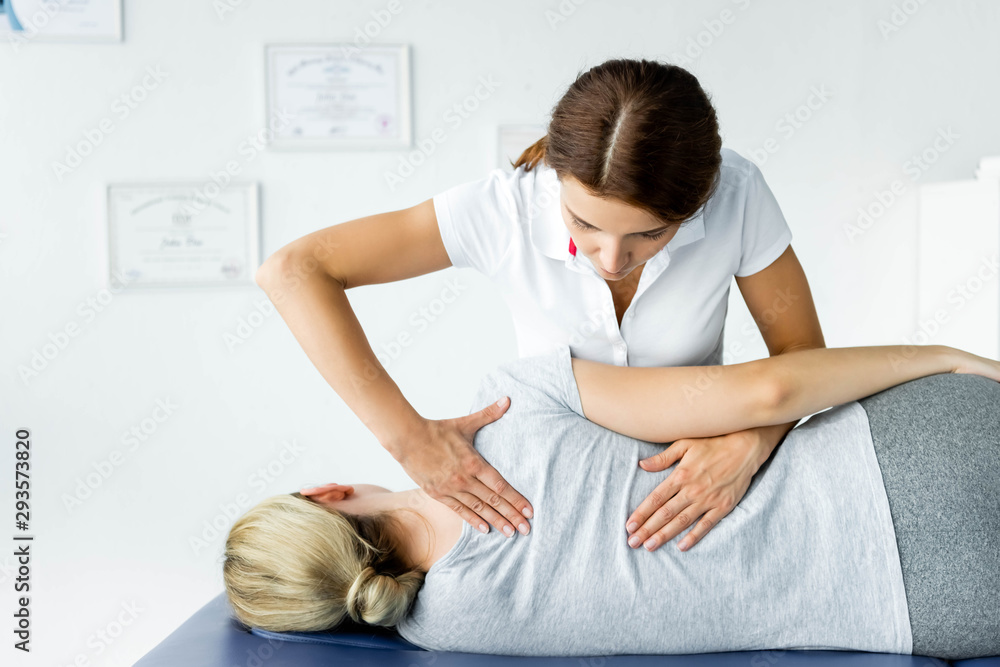 attractive chiropractor touching hand of patient in grey t-shirt attractive chiropractor touching hand of patient in grey t-shirt