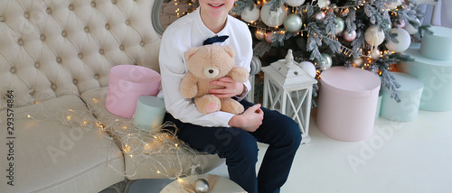 boy with a box and a bear sits on a New Year’s sofa near the Christmas tree photo