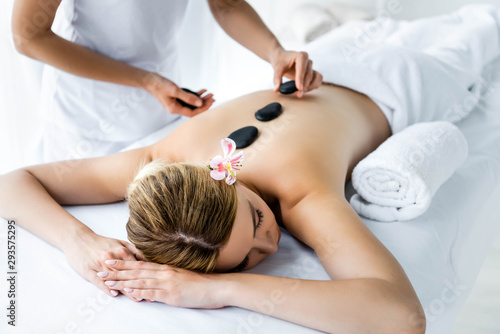 cropped view of masseur doing hot stone massage to woman in spa