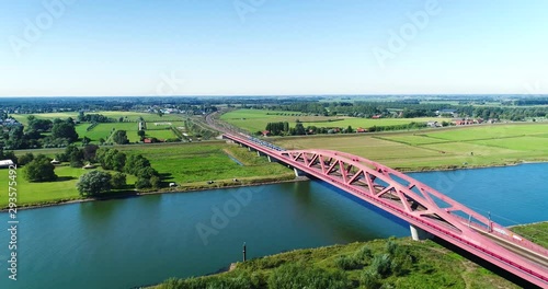 Following a Yellow and Blue Sprinter Train Crossing the Hanzeboog Bridge Over the Dutch IJssel River, The Netherlands, 4K Drone Footage