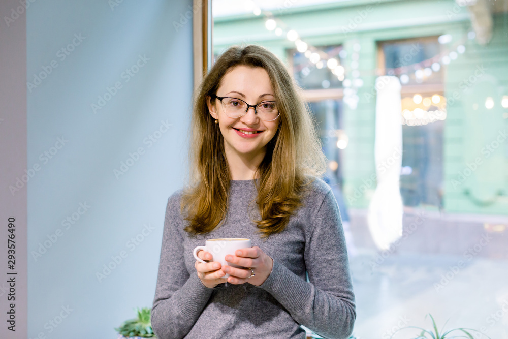 Portrait of beautiful blond woman drinking a cup of tea in cafeteria. Happy woman in a cafe drinking coffee and looking at camera. Portrait of smiling lady relaxing in a coffee shop. Portrait of beautiful blond woman drinking a cup of tea in cafeteria. Happy woman in a cafe drinking coffee and looking at camera. Portrait of smiling lady relaxing in a coffee shop.