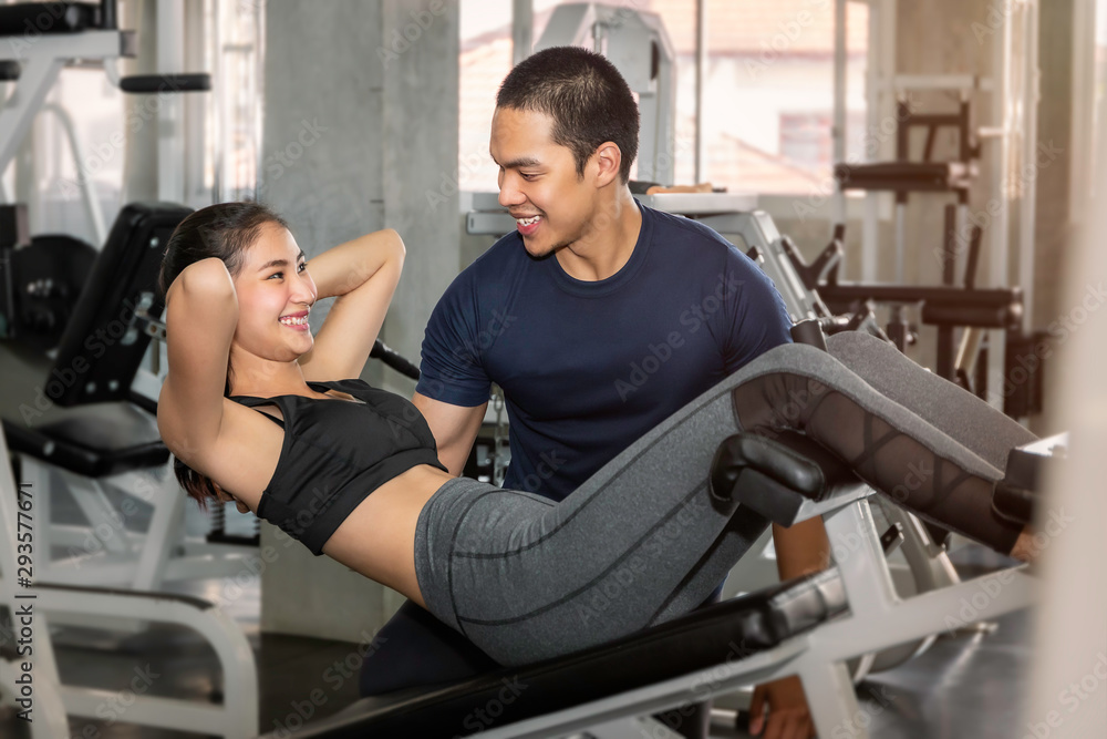 Obraz premium Young Asian woman in sportswear training sit up with male trainer at fitness gym.