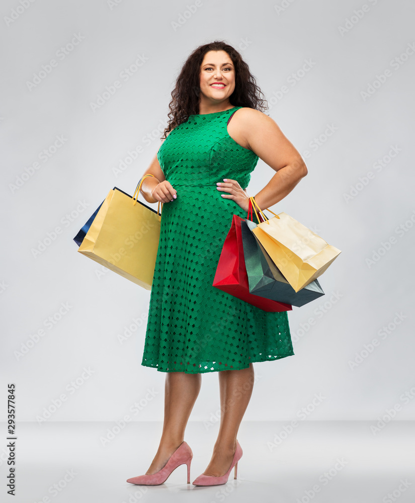 sale, outlet and consumerism concept - happy woman in green dress with shopping bags over grey background