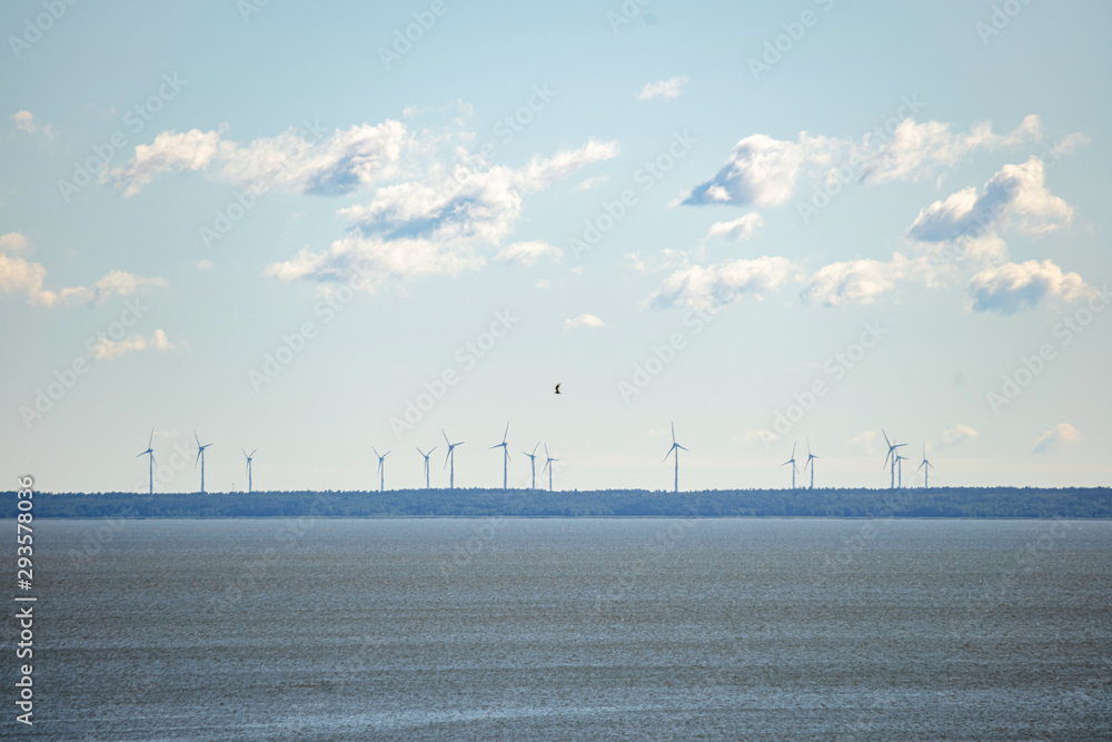 Windmills on the horizon with clouds in clear sky and sea in the foreground. Wind turbines, wind farms making electric power, green energy