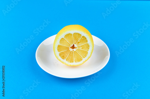 lemon on a blue background. lies on a white plate. half cut lemon. view from above. place to record. Lemon slices on a blue background. In summer, cool slices of orange. Lime, fruit, refreshing, yello