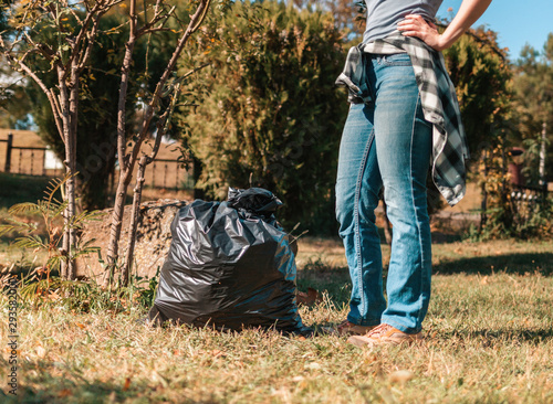 The concept of environmental pollution and Earth day. A woman volunteer removes garbage in the Park, near the feet is a black garbage bag. Close up. Tint