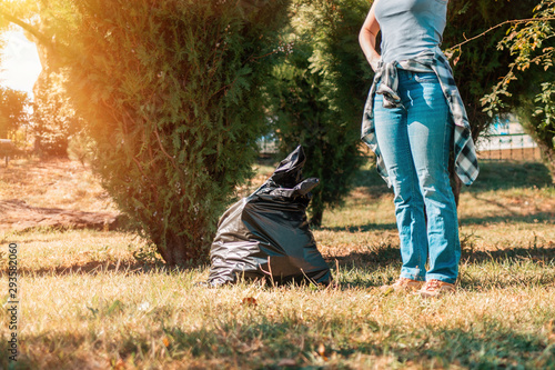 The concept of environmental pollution and Earth day. A woman volunteer removes garbage in the Park, near the feet is a black garbage bag. Copy space