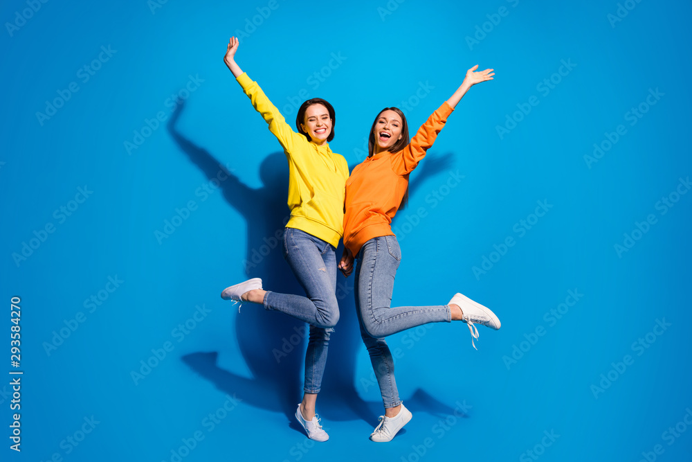 Full body photo of two pretty ladies raising arms up calling people to visit low price black friday shopping wear casual hoodies and jeans isolated blue color background