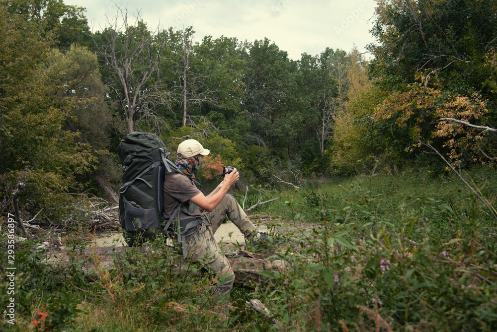 Tourist with large backpack in wilds early autumn photographs nature. Landscape with taiga forest, swamp. Hard hike walk Tourist with large backpack in wilds early autumn photographs nature. Landscape with taiga forest, swamp. Hard hike walk