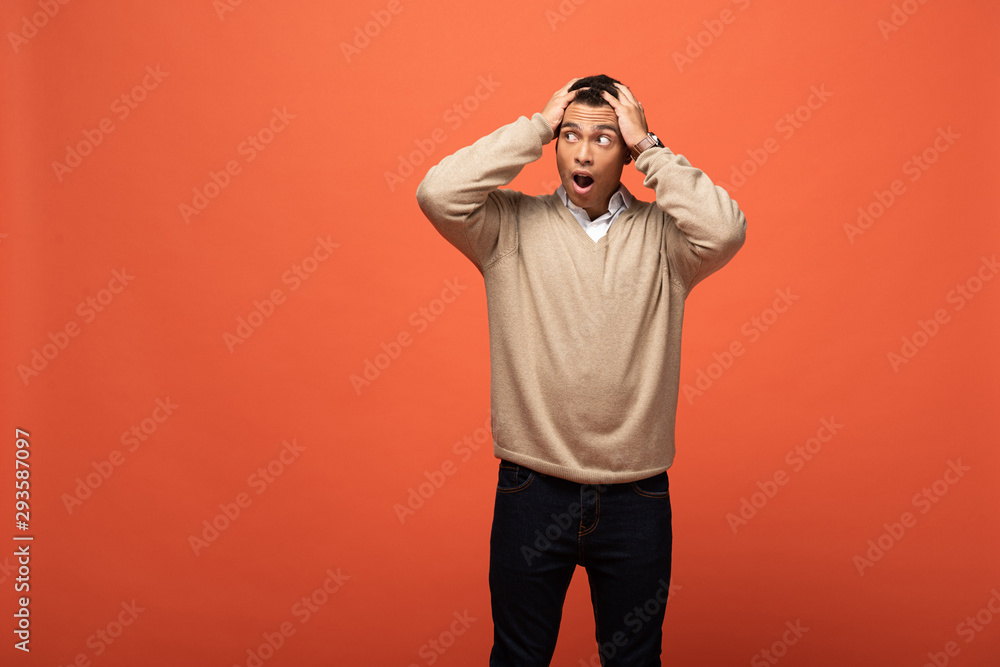 shocked mixed race man in beige sweater holding head isolated on orange shocked mixed race man in beige sweater holding head isolated on orange
