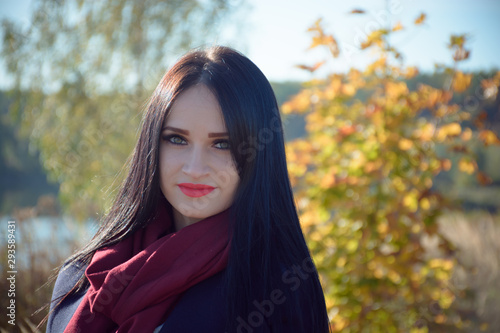 Young beautiful brunette women in positive mood wearing in dark coat and scarf in the autumn park on colorful leaves background. Bright sunny day. Romantic autumnal portrait.