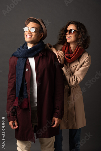 smiling stylish interracial couple in autumn outfit looking away on black background