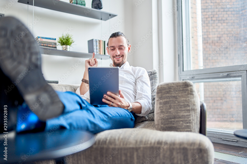 Photo of happy businessman sitting on sofa with tablet in his hands in room. Photo of happy businessman sitting on sofa with tablet in his hands in room.