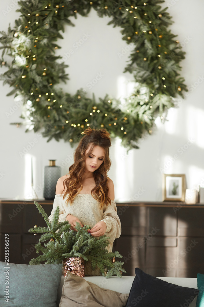 Sexy model girl with modish hairstyle and bright makeup in sweater keeping silver vase with fir branches and posing in Christmas interior Sexy model girl with modish hairstyle and bright makeup in sweater keeping silver vase with fir branches and posing in Christmas interior