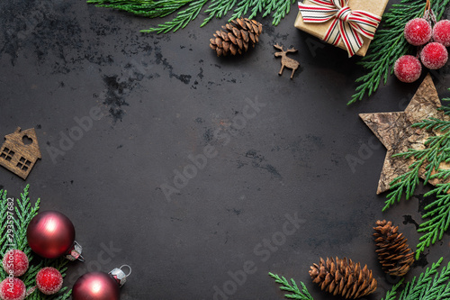 Christmas composition frame on a rusty background with festive decorations, xmas gift, baubles, holly, wooden ornaments and fresh thuja branches. With copy space, flat lay