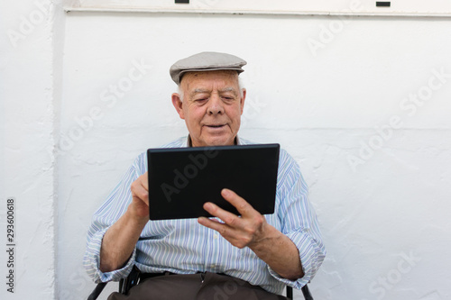 Elderly man is using a tablet in the yard of his house