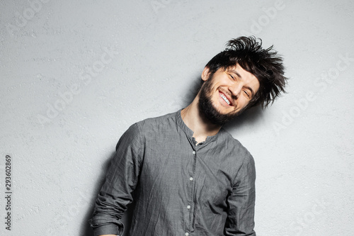 Tableau sur toile Portrait of young happy bearded guy with disheveled hair on grey background
