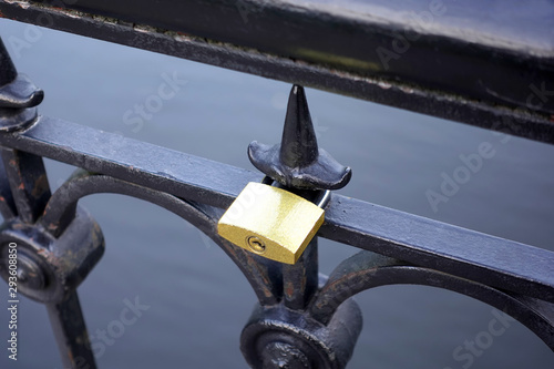 Alone golden pent padlock hangs on black metal brifge fence closeup view photo