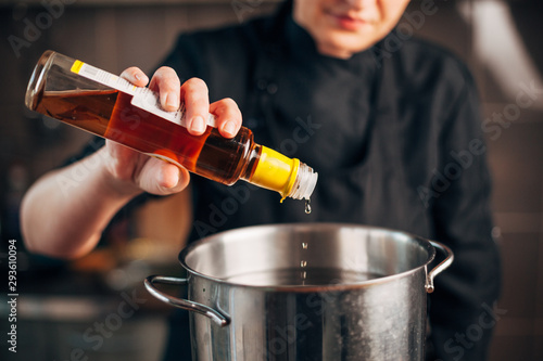 Obraz na plátně Female chef pouring vinegar in a pot with water