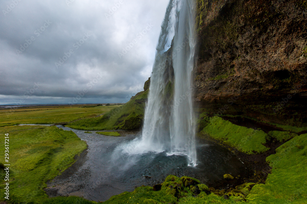 Side view of a beautiful waterfall. Water falls from a cliff in a small body of water against a cloudy sky