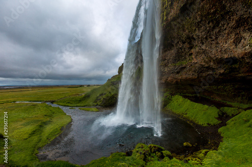 Side view of a beautiful waterfall. Water falls from a cliff in a small body of water against a cloudy sky