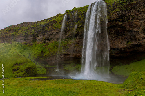 Front view of the waterfall. Water falls from rocks that are overgrown with green grass.