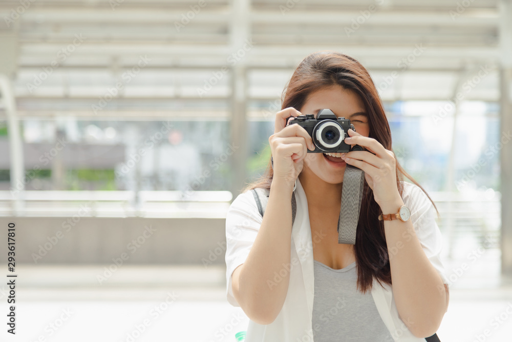 Lovely long hair Asian woman in white shirt and backpack standing shoting a photo from her camera
