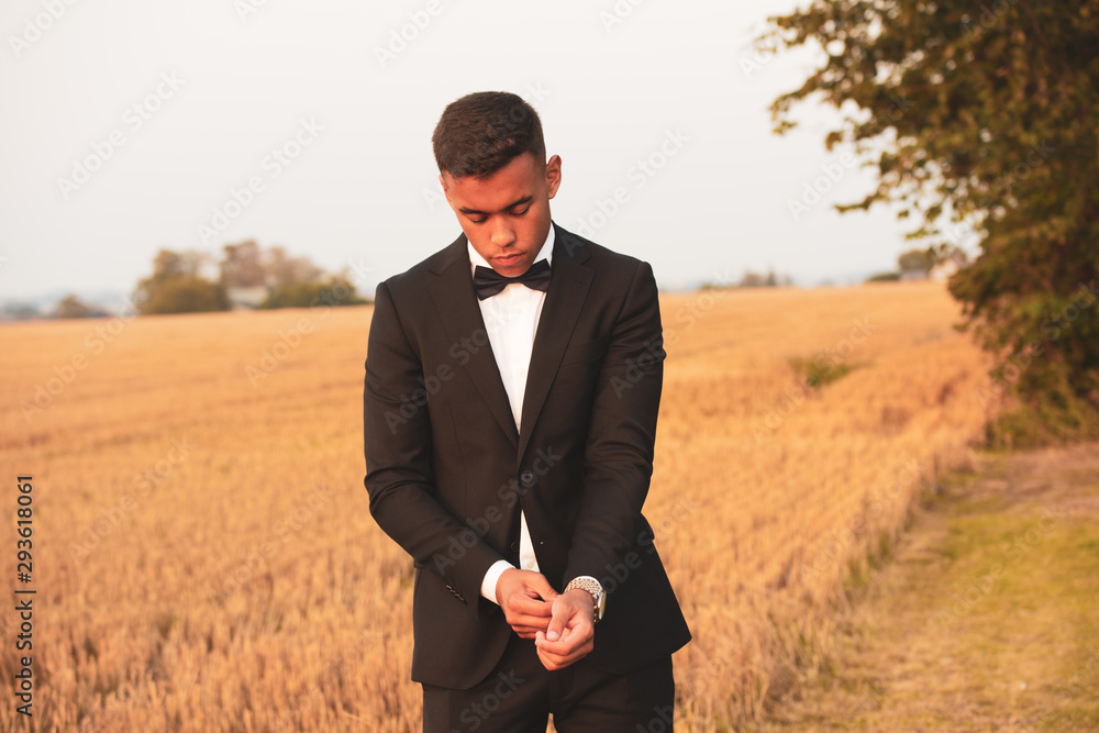 A handsome teenager dressed in black suit and bow tie and looks serious, He stands on a field that has recently been harvested in the sunset A handsome teenager dressed in black suit and bow tie and looks serious, He stands on a field that has recently been harvested in the sunset