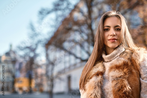 closeup portrait of beautiful young woman in warm sweater posing outdoors in city at sunny autumn day photo