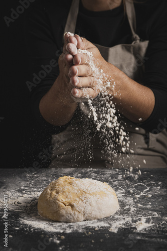 Close-up baker spreading flour on top of dough