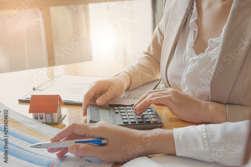 Cropped image of real estate agent assisting client to sign contract paper at desk with house model