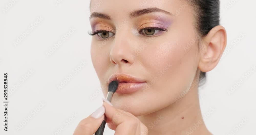 Make-up artist puts a shiny lipstick on lips. Applying makeup. Face closeup of a girl which is applied the lipstick to lips with the brush. Professional model. Real time 59.94 fps. Professional light Make-up artist puts a shiny lipstick on lips. Applying makeup. Face closeup of a girl which is applied the lipstick to lips with the brush. Professional model. Real time 59.94 fps. Professional light