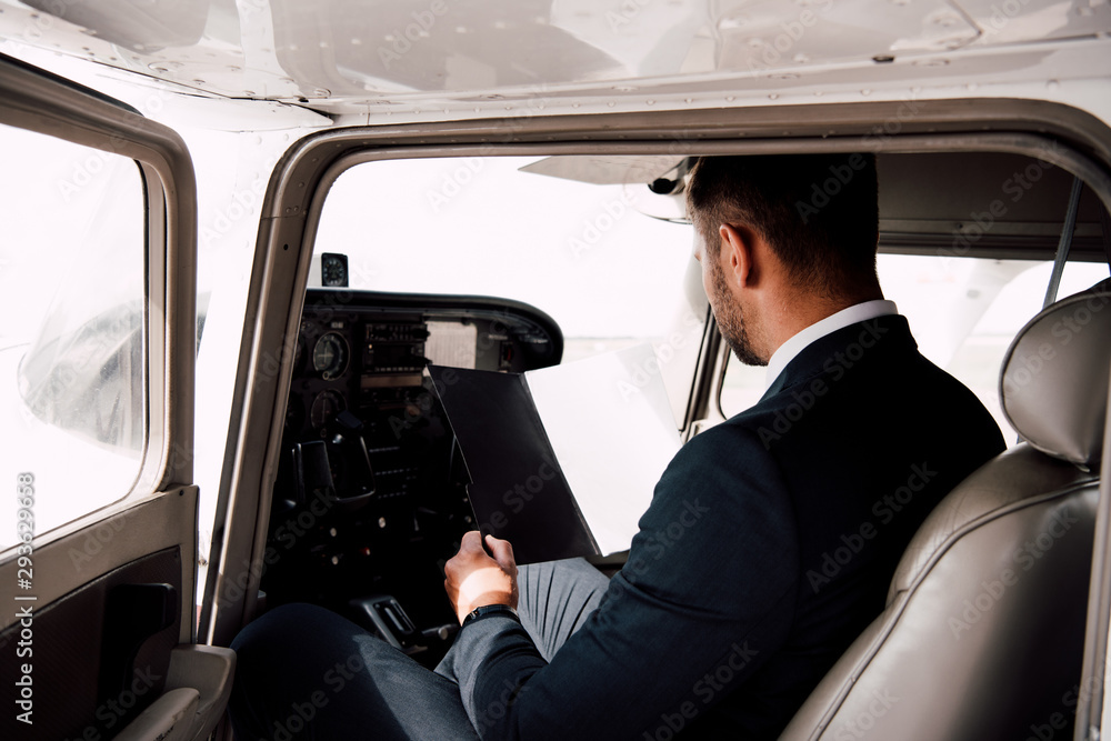 businessman in formal wear sitting in plane and holding folder