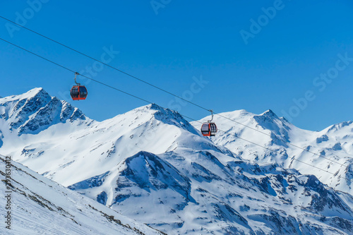 Two gondolas going up and down above the snow caped mountains. Gondolas are moving on thick ropes hanging very high. In the back there are tall Alps. Ski resort in Heiligenblut, Austria.