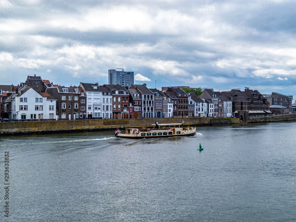 View of Meuse River with a ship and beautiful old buildings against a moody overcast sky in Maastricht, Netherlands