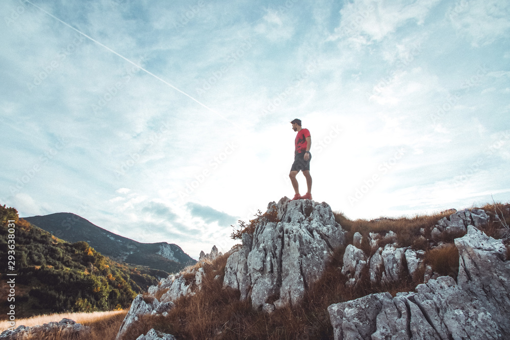 Fototapeta premium Young athletic man standing on the ridge. Trail running preparations for race.