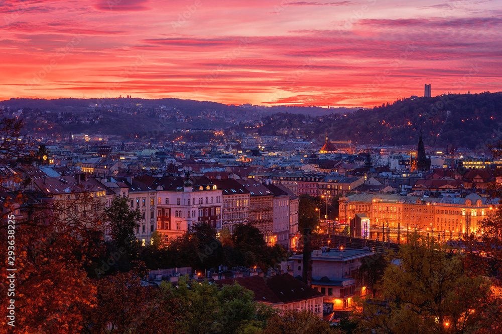 Fiery sunset view of Prague from Vitkov hill with autumn park, scenic cytiscape with city lights, Zizkov district, Czech Republic, travel background