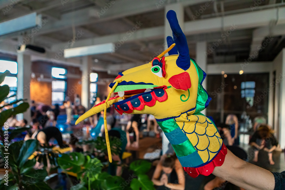 Naklejka premium Diverse group of people in yoga class. A close up and side profile view of a hand puppet on the arm of a person, a colorful and fun dragon's head used to motivate people during grueling gym workout.