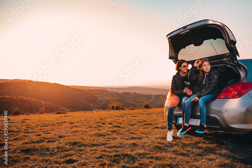 Mother and daughter sitting in car trunk on a hill and talking