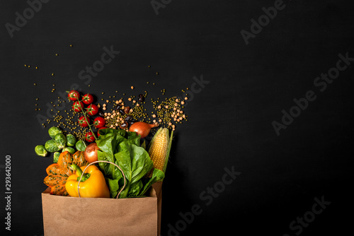 Shopping paper bag full of different fresh vegetables on a black background. Purchases concept. Healthy food organic selection. Top view. Copy space for text.