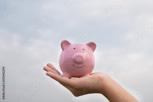 woman hand holding Pink piggy bank on sky background, step up growing business to success and saving for retirement  concept © Orathai