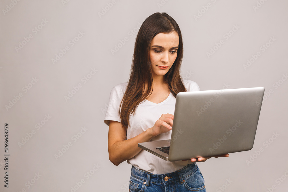 Young beautiful woman in casual clothes holding laptop and sending email to her best friend isolated over grey background. Young beautiful woman in casual clothes holding laptop and sending email to her best friend isolated over grey background.