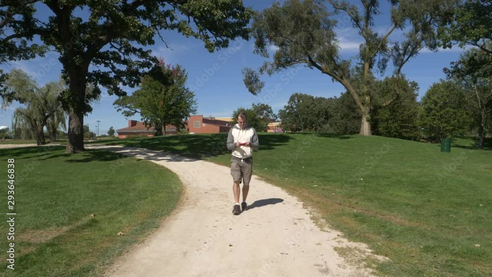 Man walking and texting on a path outdoors on a sunny fall, spring day, in the park. Man walking and texting on a path outdoors on a sunny fall, spring day, in the park.