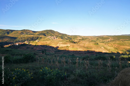 Typical Madagascar landscape in region near Alakamisy Ambohimaha, sun setting down over small clay houses, terraced rice fields in foreground and small hills background