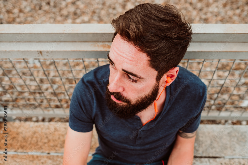 Young and handsome man with beard wearing jeans enjoying a relaxed afternoon outdoors. Texting and listening to music with his smartphone, distracted and carefree. Lifestyle. Young and handsome man with beard wearing jeans enjoying a relaxed afternoon outdoors. Texting and listening to music with his smartphone, distracted and carefree. Lifestyle.